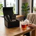 Schwarze Geschenkbox mit Teedosen und Teebeuteln, offen auf dem Tisch mit Tasse