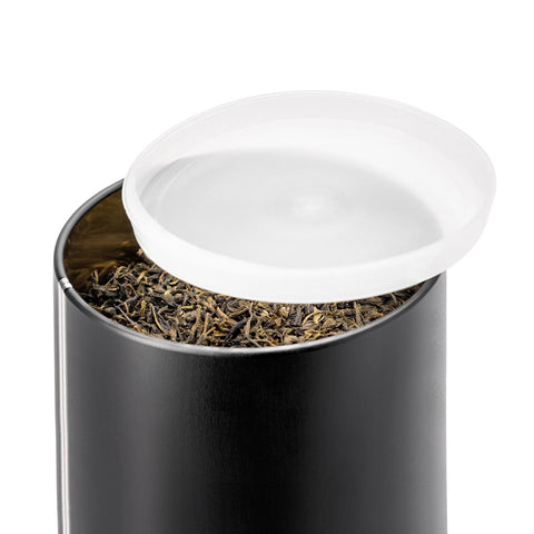 Schwarze Teedose mit geöffnetem Deckel, Blick ins Innere mit Teeblättern