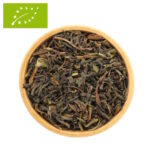 Eine Holzschale, gefüllt mit losem Bio Darjeeling First Flush Tee. Die getrockneten Teeblätter zeigen eine charakteristische Mischung aus dunkelgrünen und braunen Nuancen mit vielen hellen, silbrigen Blattspitzen.
