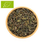 Eine Holzschale, gefüllt mit losem Bio Darjeeling First Flush Tee. Die getrockneten Teeblätter zeigen eine charakteristische Mischung aus dunkelgrünen und braunen Nuancen mit vielen hellen, silbrigen Blattspitzen.